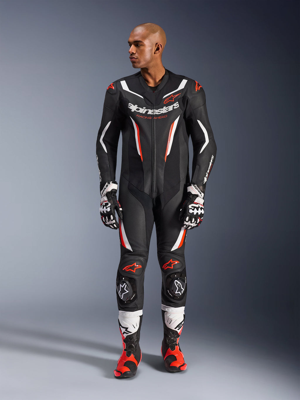 Alpinestars GP Force V2 Leather Suit - 1 pièce, noir, blanc et rouge fluo, vue en pied d'un mannequin portant un équipement de course de moto professionnel avec gants et bottes assortis, dotée de panneaux en cuir perforé et de sliders de genou.