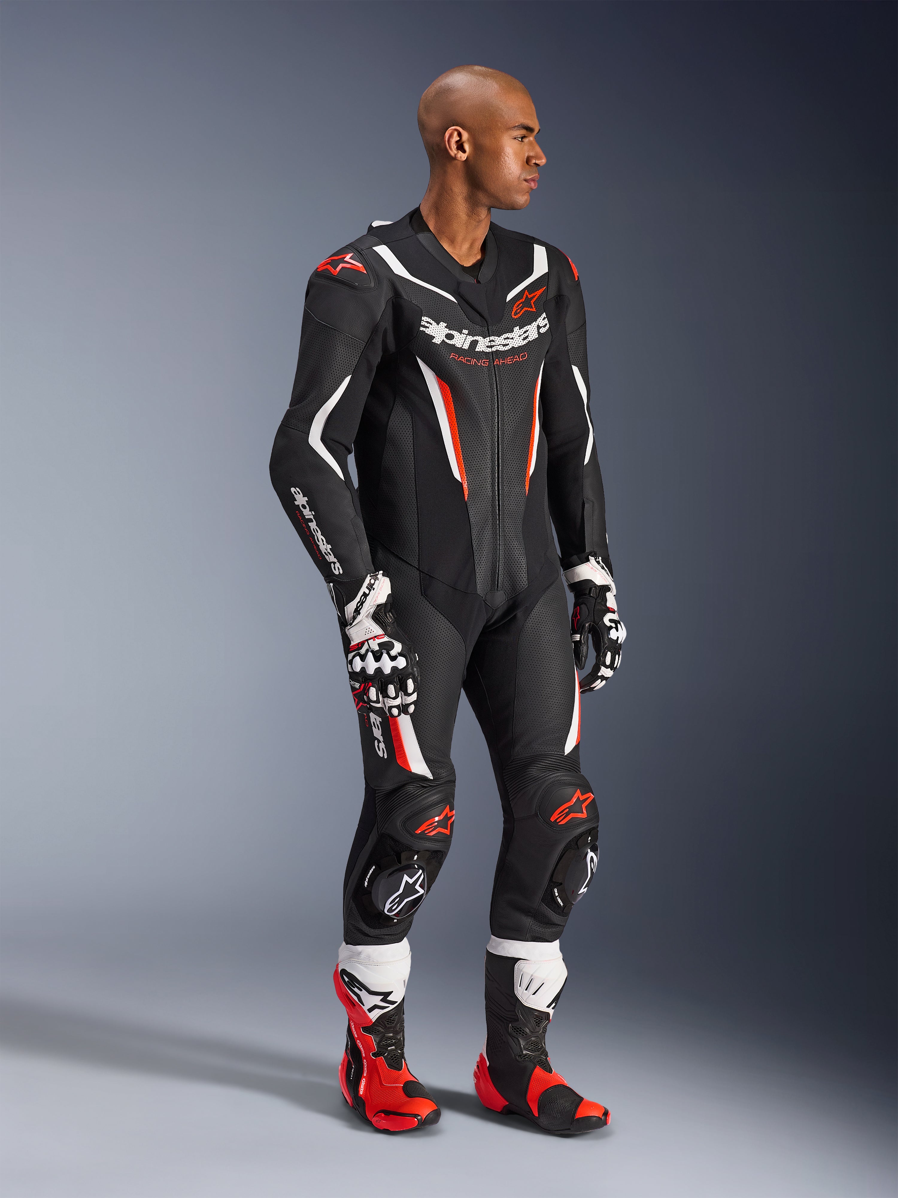 Combinaison en cuir Alpinestars GP Force V2 - 1 pièce, Noir Blanc et Rouge Fluo, portée avec des gants et des bottes de course assortis, dotée de panneaux en cuir perforé, d'accents blancs et rouges vifs et du logo Alpinestars sur la poitrine et les manches, conçue pour la performance sur circuit.