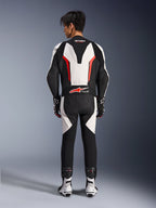 Combinaison en cuir Alpinestars GP Force V2 1 pièce, combinaison de course moto, blanc, noir et rouge fluo, vue arrière du mannequin portant la combinaison avec des bottes et des gants de course, dotée d'une bosse aérodynamique, de panneaux extensibles en accordéon et du logo Tech-Air Ready