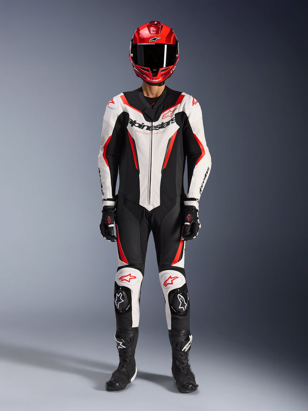 Combinaison en cuir Alpinestars GP Force V2 - 1 pièce, blanc, noir et rouge fluo, équipement de course complet avec casque rouge, gants et bottes noirs, design aérodynamique et logo Alpinestars sur la poitrine et les genoux