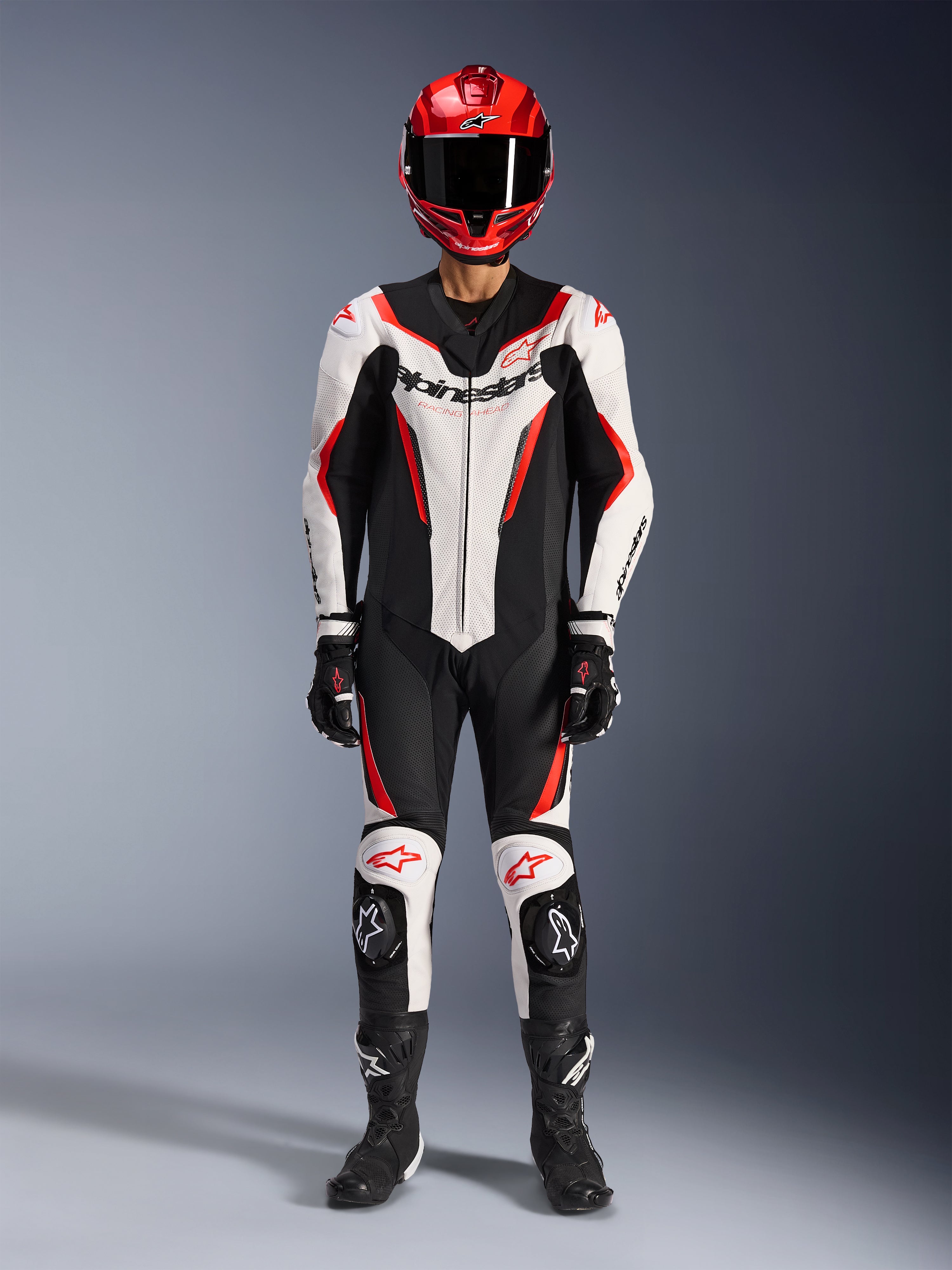 Combinaison en cuir Alpinestars GP Force V2 - 1 pièce, blanc, noir et rouge fluo, équipement de course complet avec casque rouge, gants et bottes noirs, design aérodynamique et logo Alpinestars sur la poitrine et les genoux