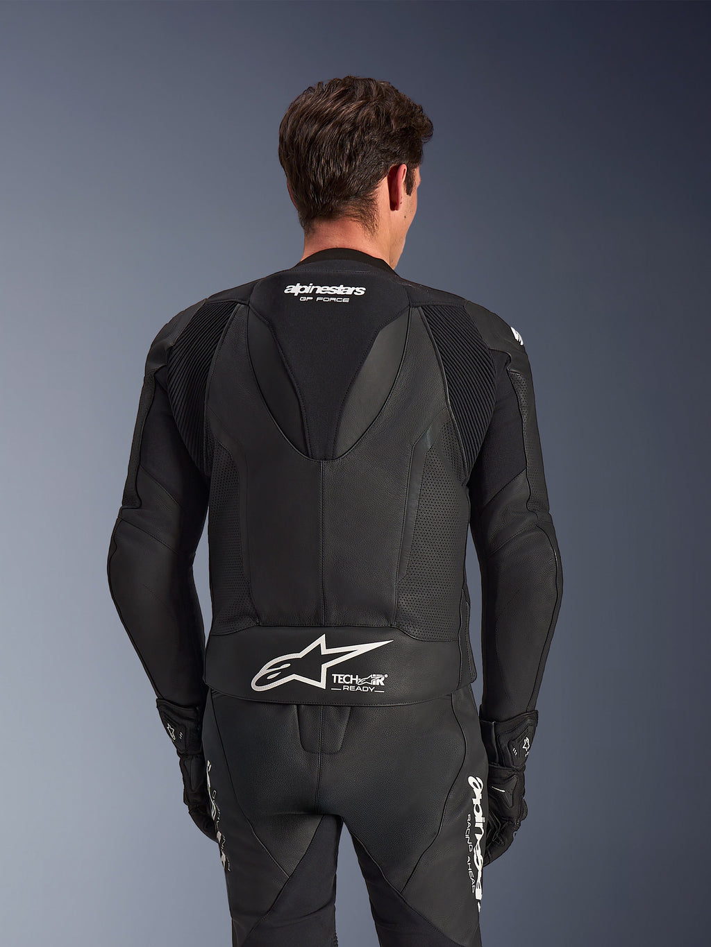 Combinaison en cuir Alpinestars GP Force V2 2 pièces, noire, vue arrière du pilote, avec panneaux en cuir perforé, bosse aérodynamique avec marquage GP Force, et logo Alpinestars blanc avec texte Tech-Air Ready en bas du dos.
