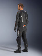 Alpinestars GP Force V2 2-teiliger Lederanzug, Schwarz mit weißen und Red Fluo Akzenten, Dreiviertel-Rückansicht am Modell, mit aerodynamischem Höcker, perforierten Ledereinsätzen und markantem Alpinestars-Branding, getragen mit schwarzen Rennstiefeln und Handschuhen.
