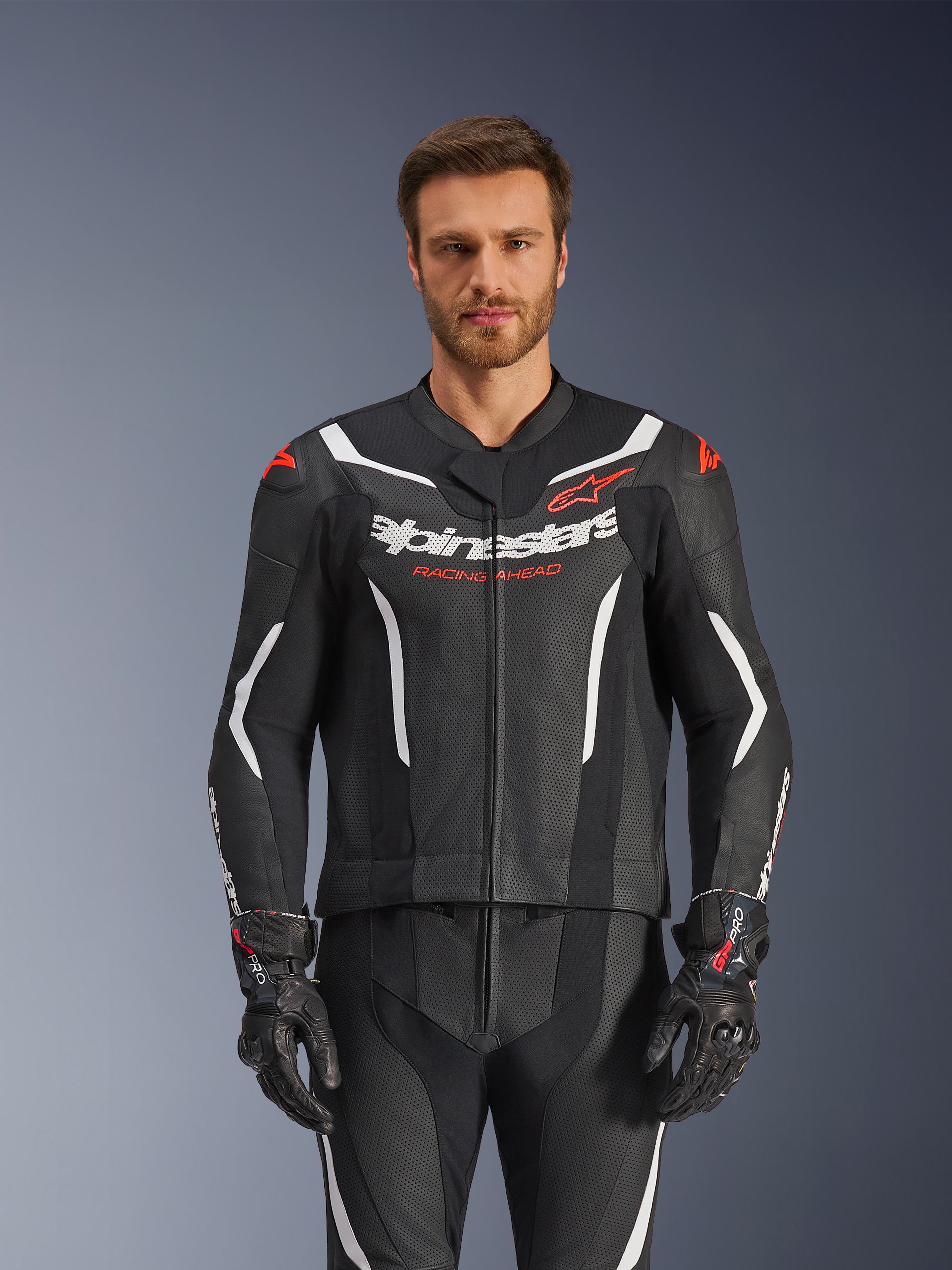 Alpinestars GP Force V2 Lederkombi – 2-teilig, Schwarz, Weiß und Fluo-Rot, Vorderansicht eines männlichen Models in der perforierten Lederkombi mit passenden schwarzen Handschuhen, mit weißen eckigen Akzenten und Alpinestars-Branding auf der Brust