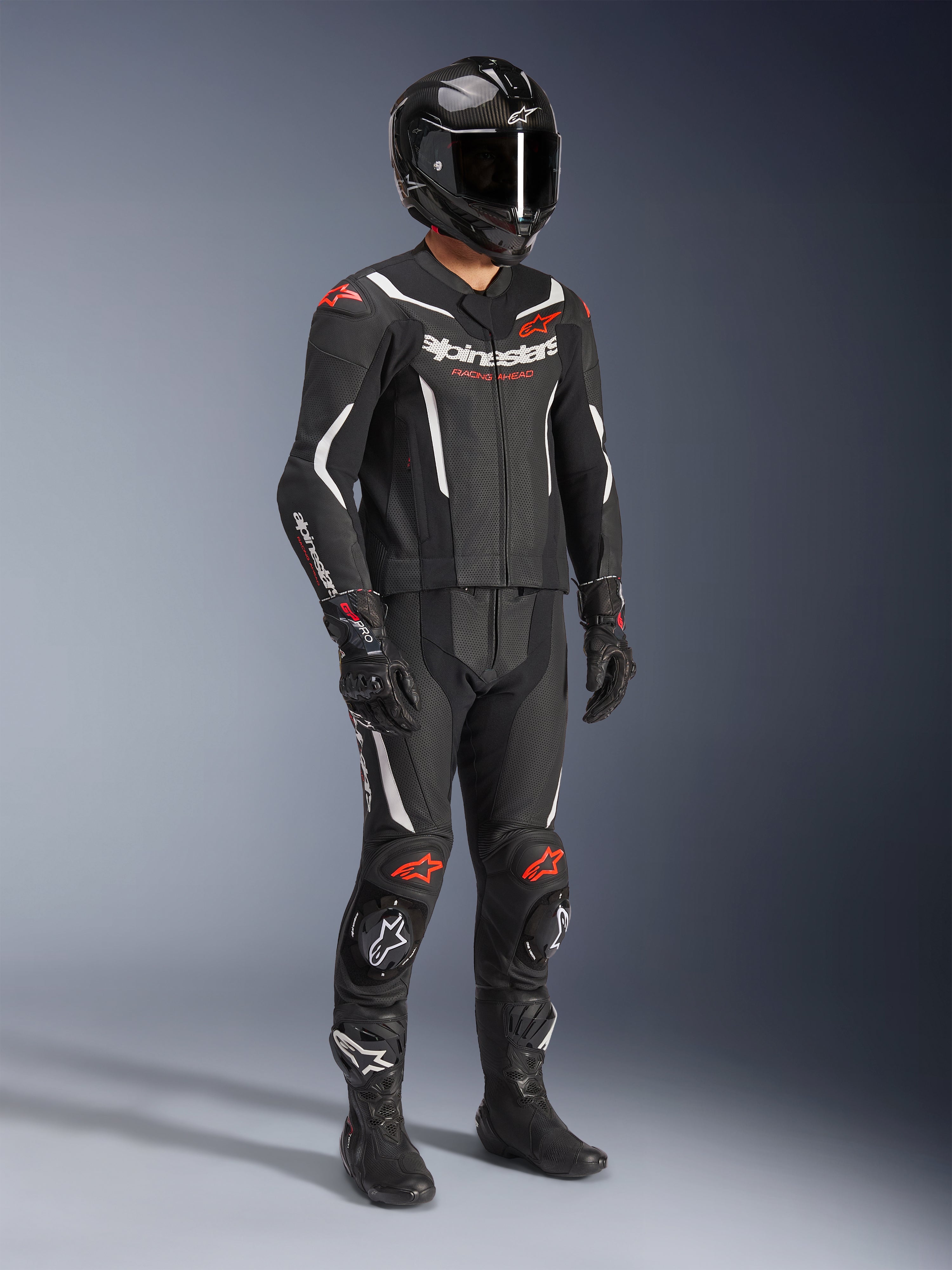 Alpinestars GP Force V2 2-teiliger Lederanzug, Schwarz, Weiß und Fluo-Rot, komplette Motorrad-Rennausrüstung mit Carbon-Helm, Rennhandschuhen und Stiefeln, Lederkonstruktion mit perforierten Einsätzen und aerodynamischem Rückenhöcker.