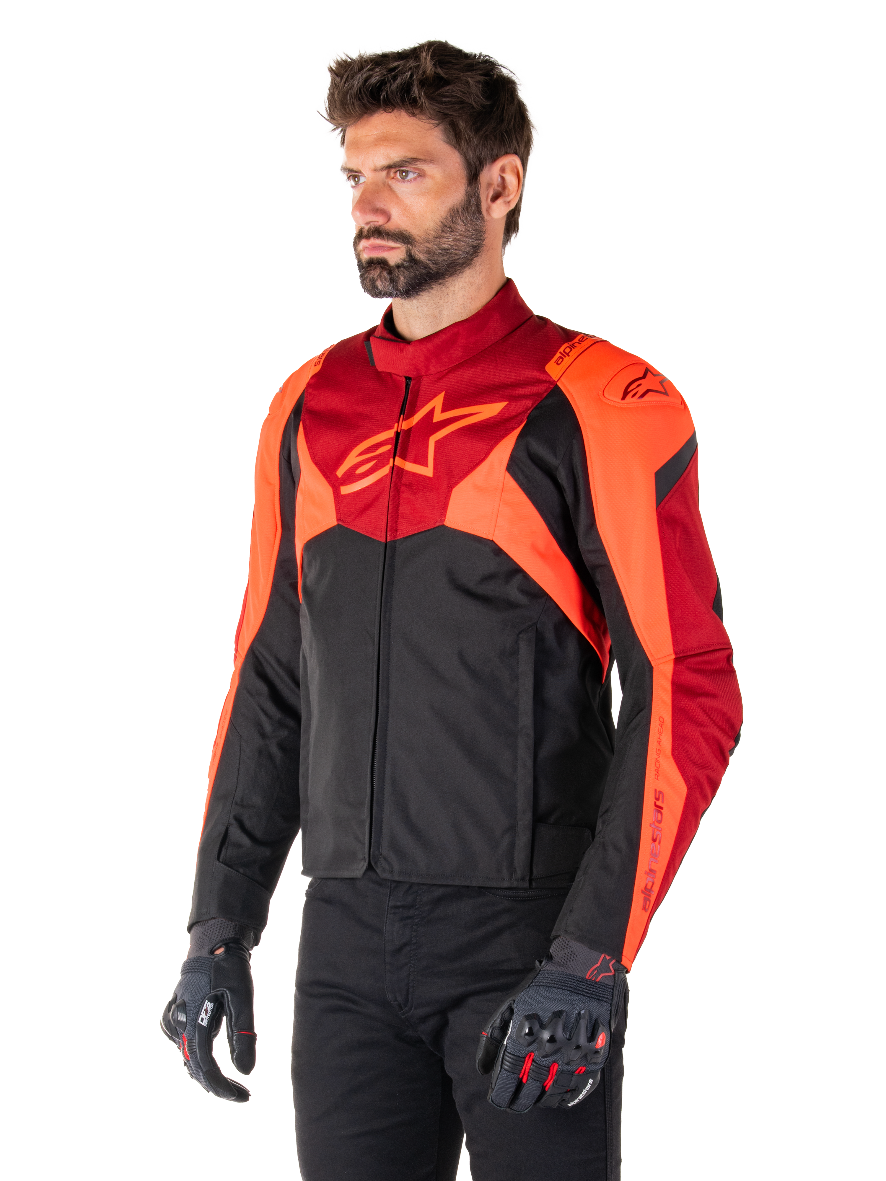 Alpinestars T-Jaws V4 Wasserdichte Jacke, Schwarz, Rot Fluo und Dunkelrot, getragen von einem männlichen Model mit schwarzer Hose und Motorradhandschuhen, aggressive sportliche Silhouette mit Alpinestars-Logo auf der Brust, Dreiviertelansicht