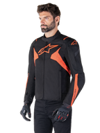 Alpinestars T-Jaws V4 Wasserdichte Jacke, Schwarz und Rot Fluo, sportliche Motorradjacke getragen von einem männlichen Model, mit markanten orangefarbenen Stern-Logos auf der Brust und den Schultern, kombiniert mit schwarzen Handschuhen und Hosen