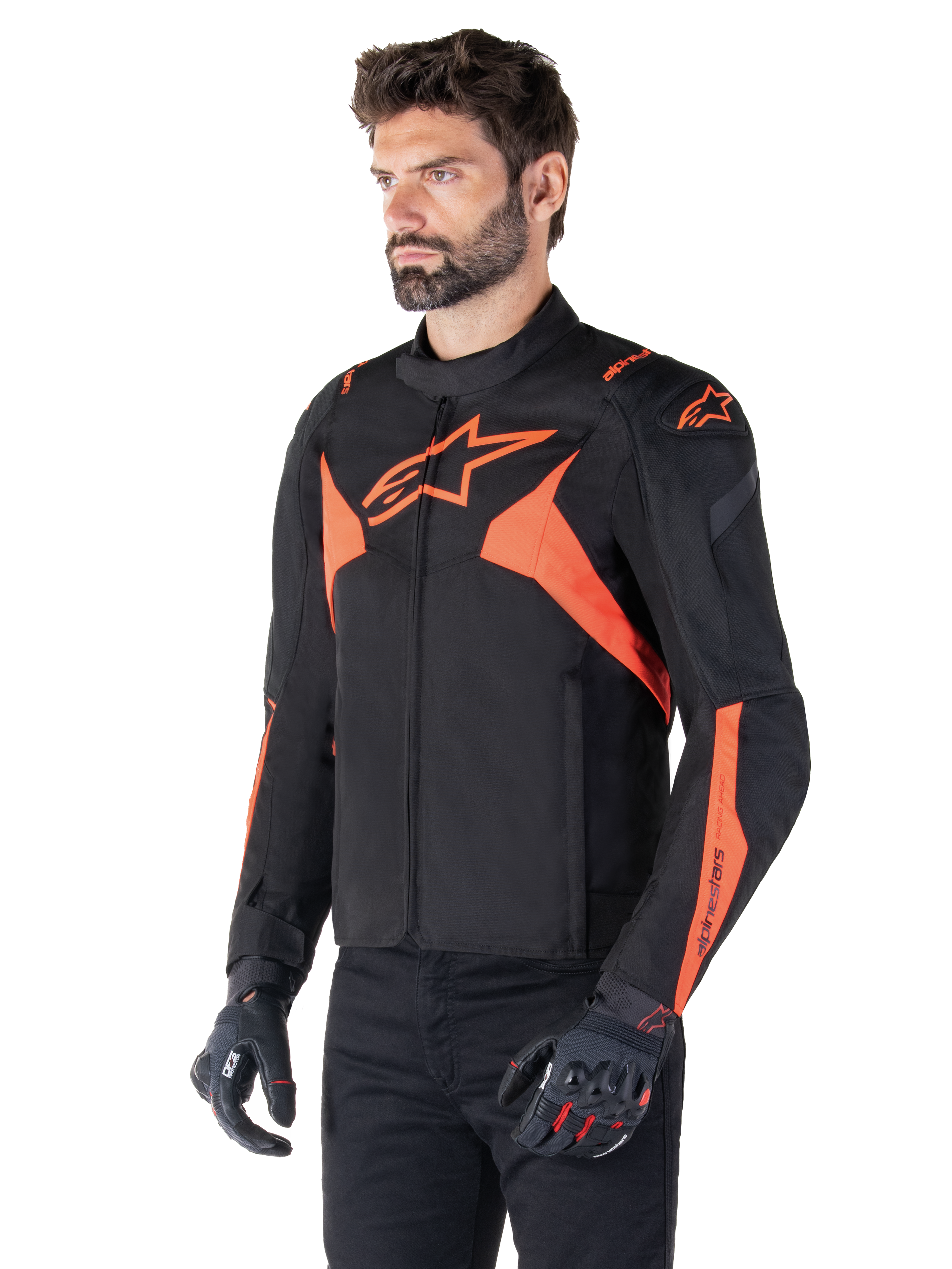 Alpinestars T-Jaws V4 Wasserdichte Jacke, Schwarz und Rot Fluo, sportliche Motorradjacke getragen von einem männlichen Model, mit markanten orangefarbenen Stern-Logos auf der Brust und den Schultern, kombiniert mit schwarzen Handschuhen und Hosen