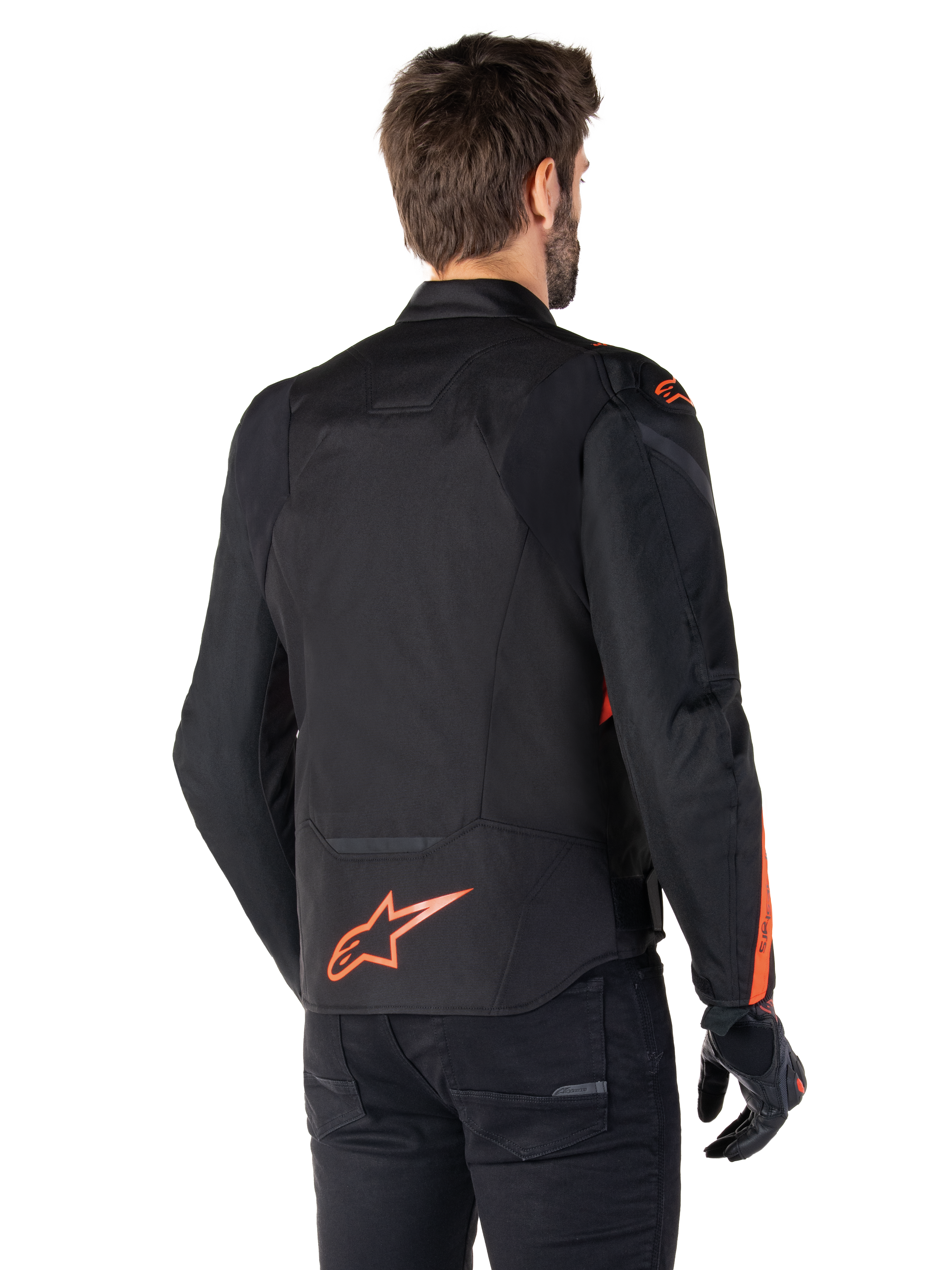 Männliches Modell in der Alpinestars T-Jaws V4 Wasserdichten Jacke in der Rückansicht, Schwarz mit Red Fluo Akzenten, mit einem Red Fluo Logo am unteren Rücken und Akzenten an den Schultern und Ärmeln, sportliche Motorradbekleidung.