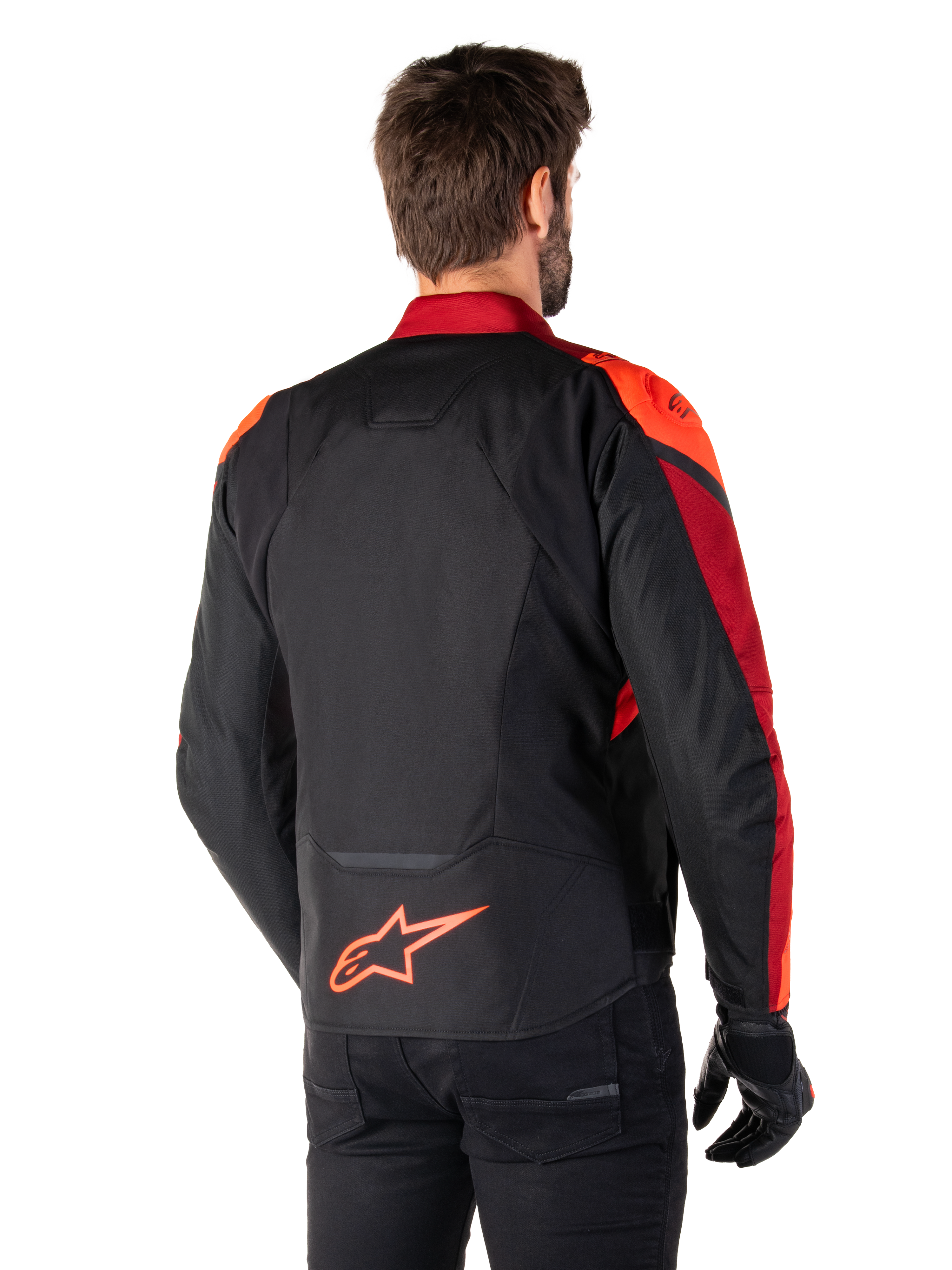 Rückansicht eines Mannes, der die Alpinestars T-Jaws V4 Wasserdichte Jacke in Schwarz Rot Fluo Dunkelrot trägt, mit leuchtend roten Akzenten an den Schultern und Ärmeln, einem fluoreszierend roten Alpinestars-Logo auf dem unteren Rücken, kombiniert mit einer schwarzen Hose und Handschuhen.