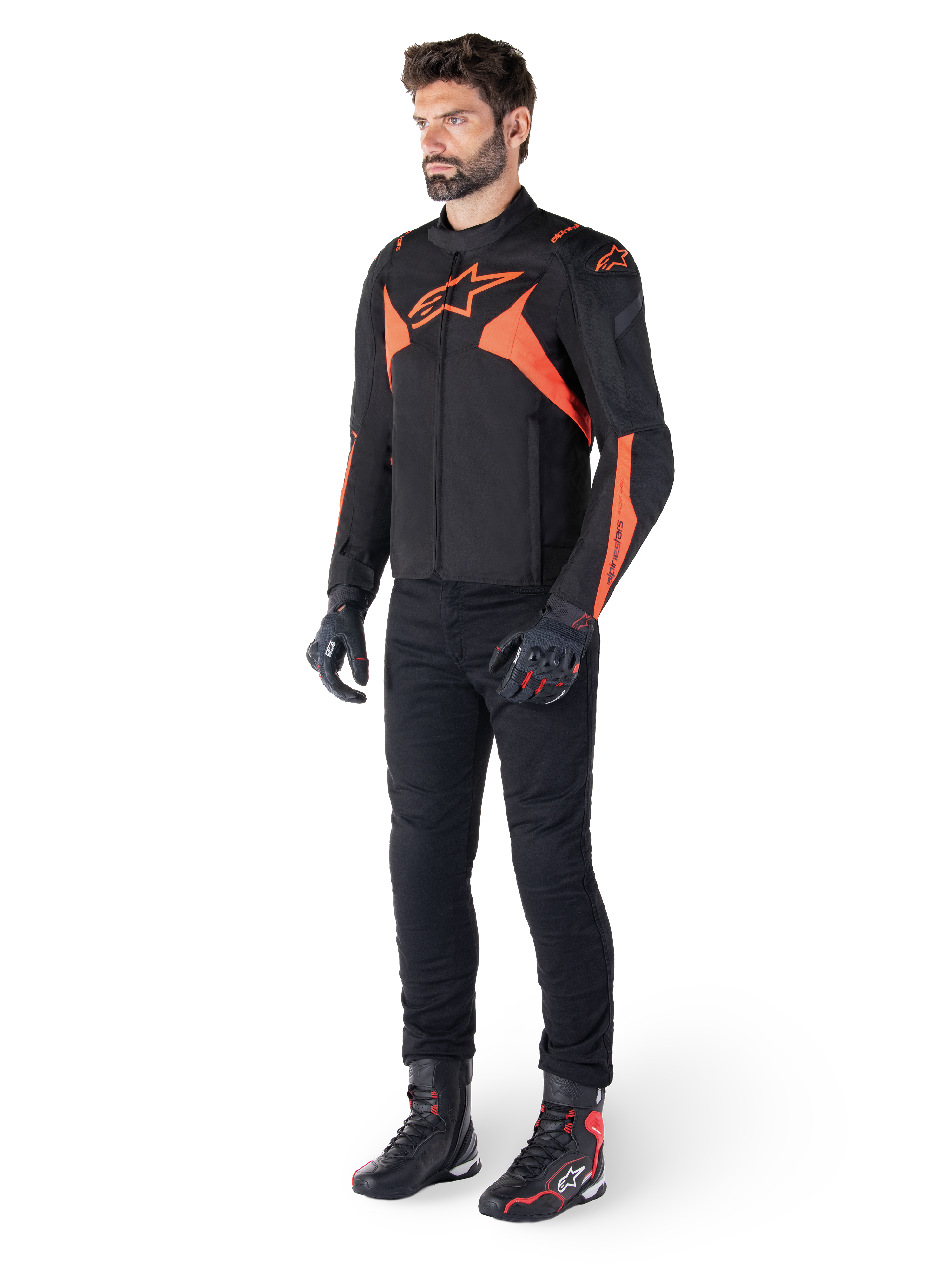 Alpinestars T-Jaws V4 Wasserdichte Jacke, Schwarz und Rot Fluo, getragen von einem männlichen Model mit schwarzer Hose, Handschuhen und Stiefeln, mit leuchtend orangefarbenen Akzenten und dem Alpinestars-Logo, sportliches Design für das Motorradfahren