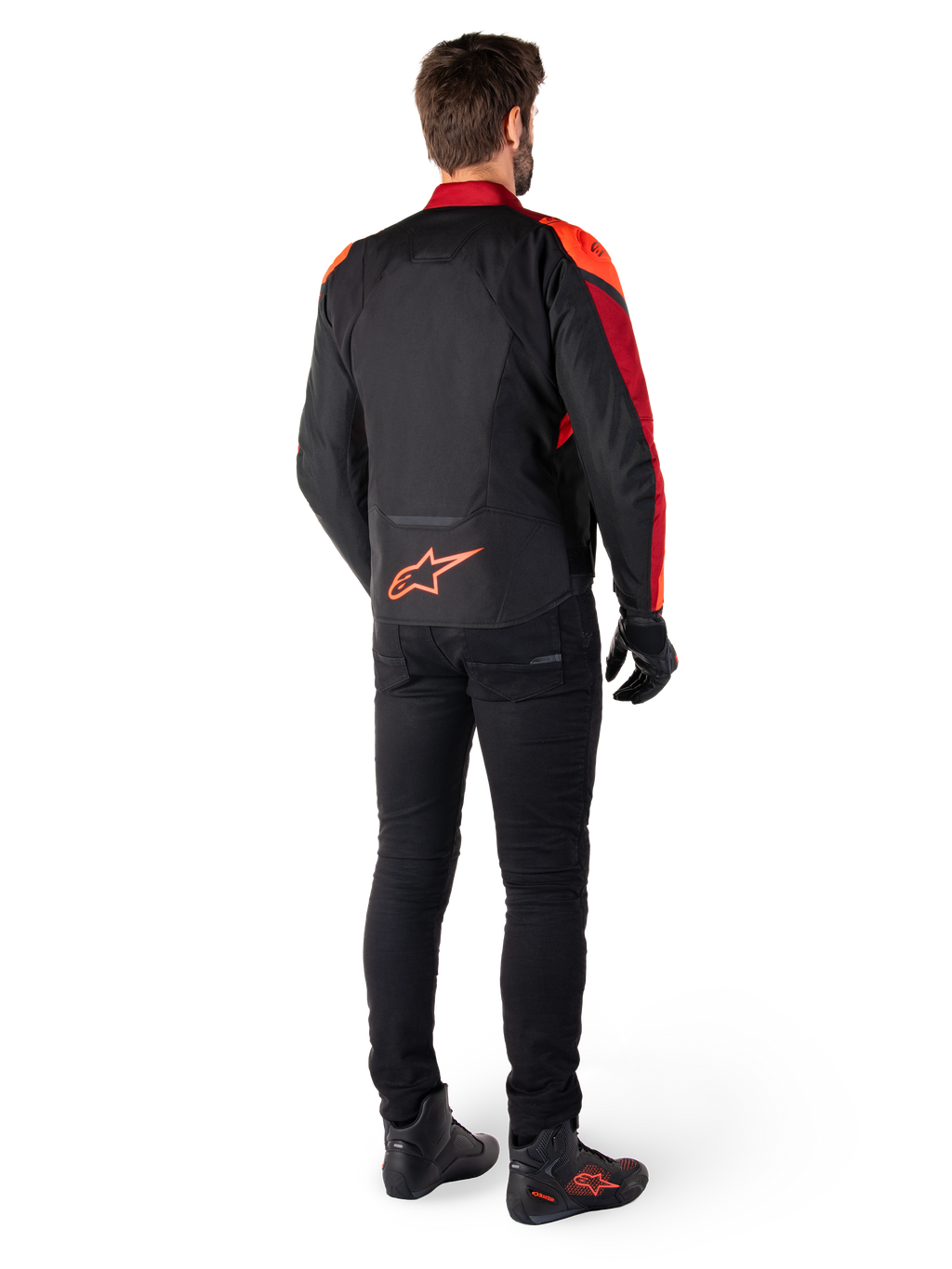 Alpinestars T-Jaws V4 Wasserdichte Jacke in Schwarz Rot Fluo Dunkelrot, Rückansicht eines Fahrers, der die Textiljacke mit schwarzer Hose und Motorradstiefeln trägt, mit einem markanten roten Alpinestars-Logo auf dem unteren Rücken.