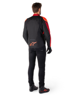 Alpinestars T-Jaws V4 Wasserdichte Jacke in Schwarz Rot Fluo Dunkelrot, Rückansicht eines Fahrers, der die Textiljacke mit schwarzer Hose und Motorradstiefeln trägt, mit einem markanten roten Alpinestars-Logo auf dem unteren Rücken.