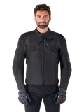 Alpinestars T-Jaws V4 Wasserdichte Jacke, schwarze Motorrad-Sportjacke, getragen von einem Mann mit schwarzen Handschuhen mit roten Akzenten, verstärkte Schultern und Arme, elegantes Design mit dezentem Brustlogo, textile Allwetter-Fahrerausrüstung