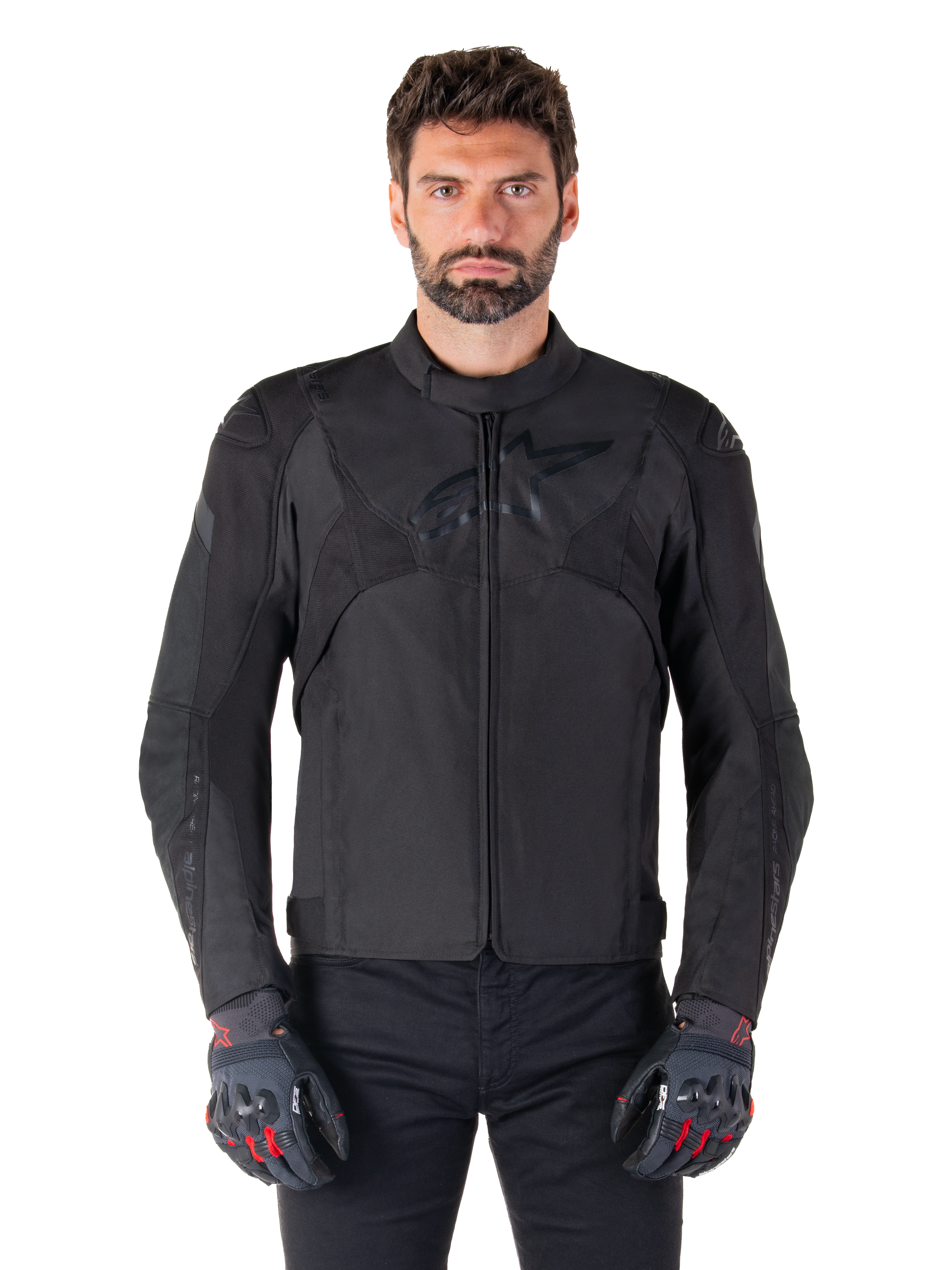 Alpinestars T-Jaws V4 Wasserdichte Jacke, schwarze Motorrad-Sportjacke, getragen von einem Mann mit schwarzen Handschuhen mit roten Akzenten, verstärkte Schultern und Arme, elegantes Design mit dezentem Brustlogo, textile Allwetter-Fahrerausrüstung