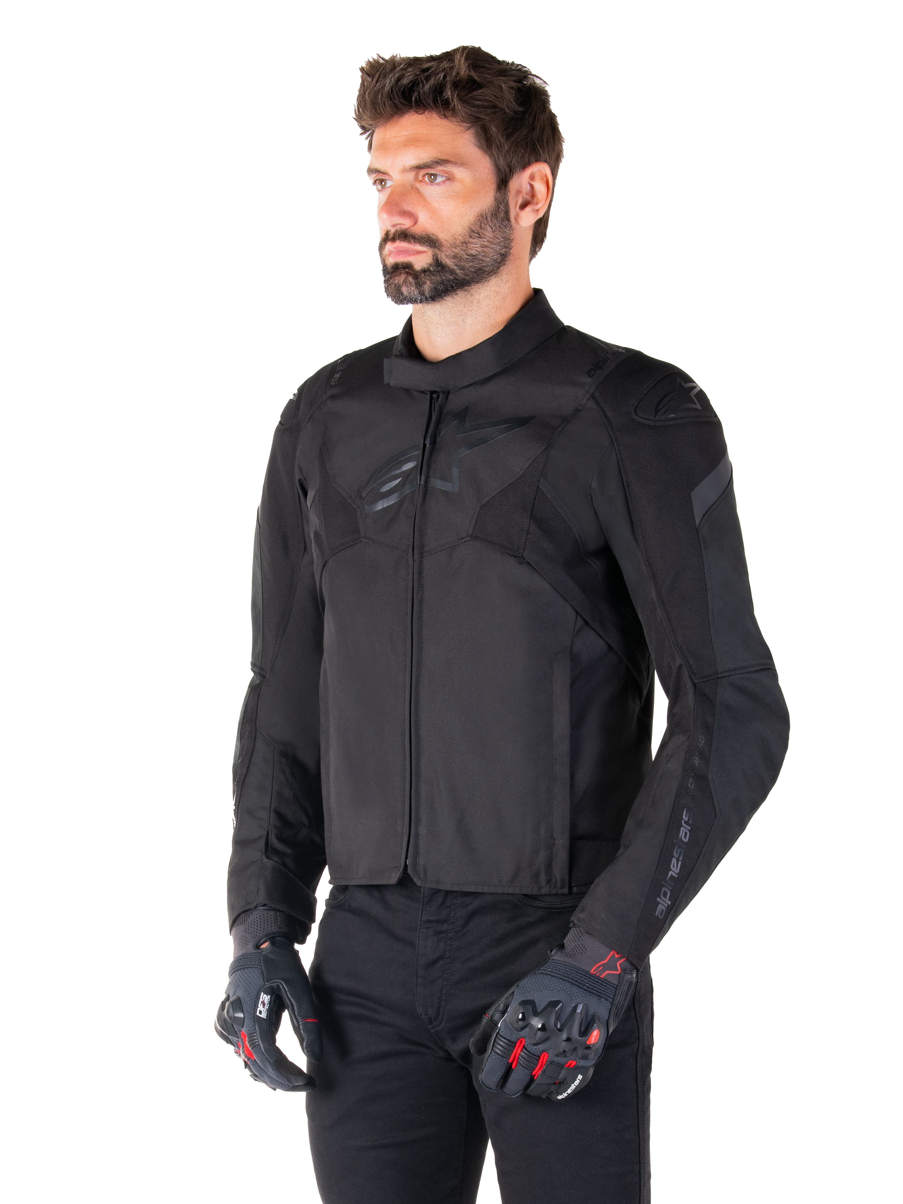 Männlicher Fahrer in der wasserdichten Alpinestars T-Jaws V4 Jacke in Schwarz, kombiniert mit einer schwarzen Hose und Schutzhandschuhen, mit einer schlanken sportlichen Passform, tonalen Alpinestars-Logos auf der Brust und den Schultern sowie einer leistungsstarken Textilkonstruktion.