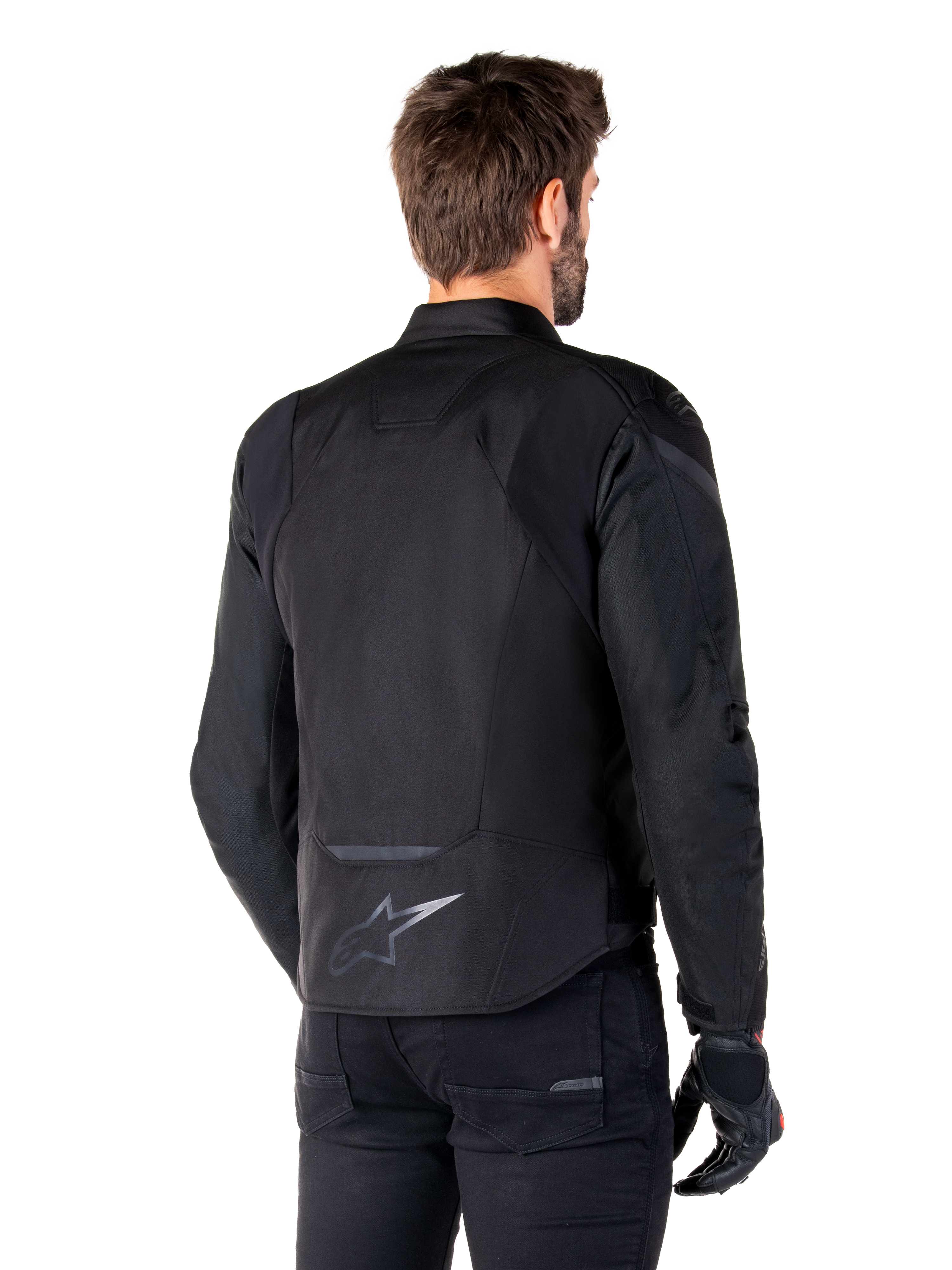 Alpinestars T-Jaws V4 Wasserdichte Jacke, Schwarz, Rückansicht am Modell, mit reflektierendem Alpinestars-Logo am unteren Rücken, verlängerte Rückenpartie für mehr Abdeckung, sportliches Textildesign mit farblich abgestimmten Einsätzen, getragen mit schwarzen Motorradhandschuhen