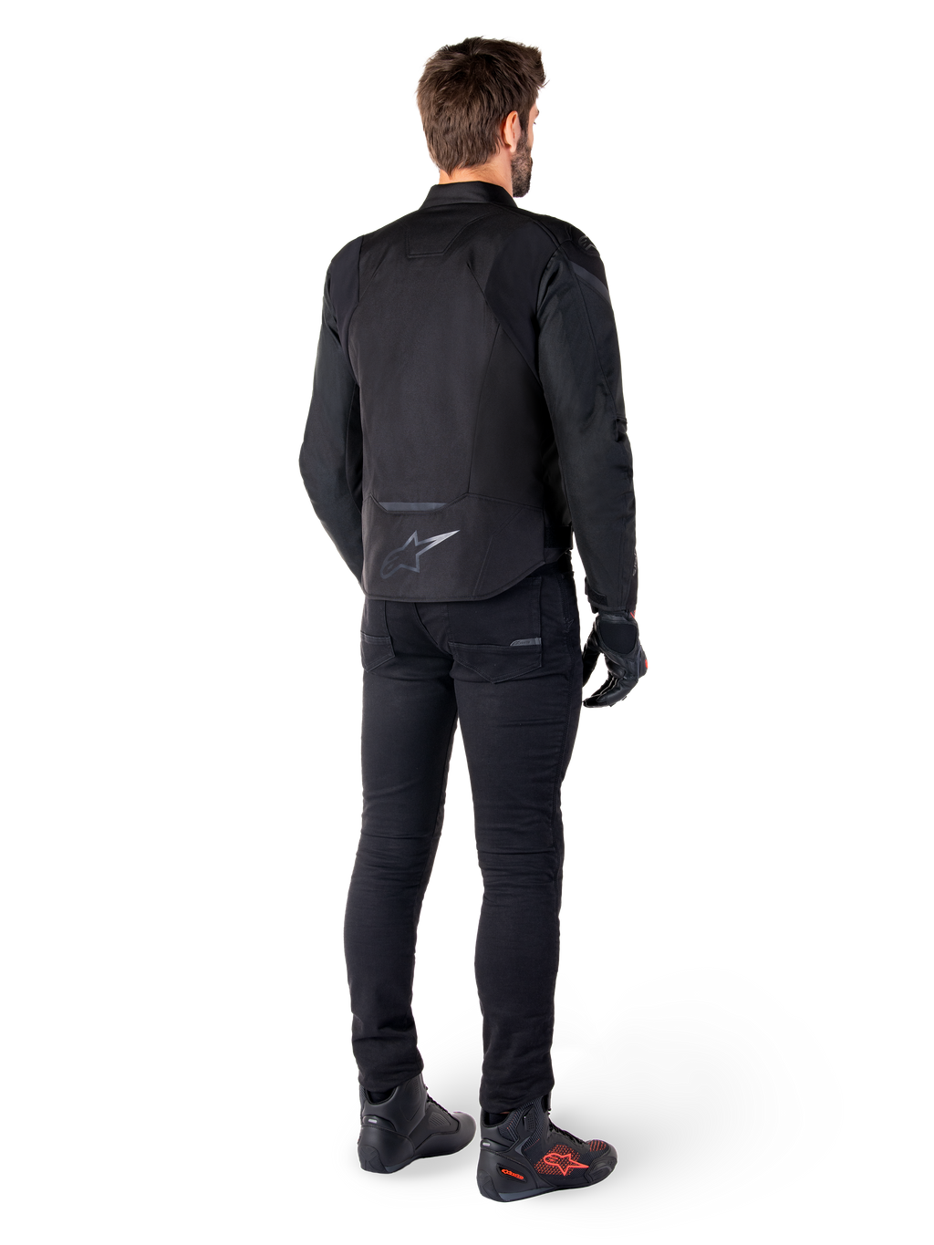 Alpinestars T-Jaws V4 Wasserdichte Jacke, Schwarz, Rückansicht am Modell mit schwarzer Motorradhose und Stiefeln, zeigt die sportliche Textilkonstruktion und das Alpinestars-Logo am unteren Rücken.