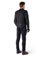 Alpinestars T-Jaws V4 Wasserdichte Jacke, Schwarz, Rückansicht am Modell mit schwarzer Motorradhose und Stiefeln, zeigt die sportliche Textilkonstruktion und das Alpinestars-Logo am unteren Rücken.