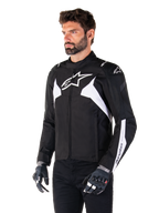 Alpinestars T-Jaws V4 Waterproof Jacket, zwart en wit, gedragen door een model met motorhandschoenen, met opvallende witte Alpinestars-logo's en accenten, sportieve textiele motorjas voor op de weg