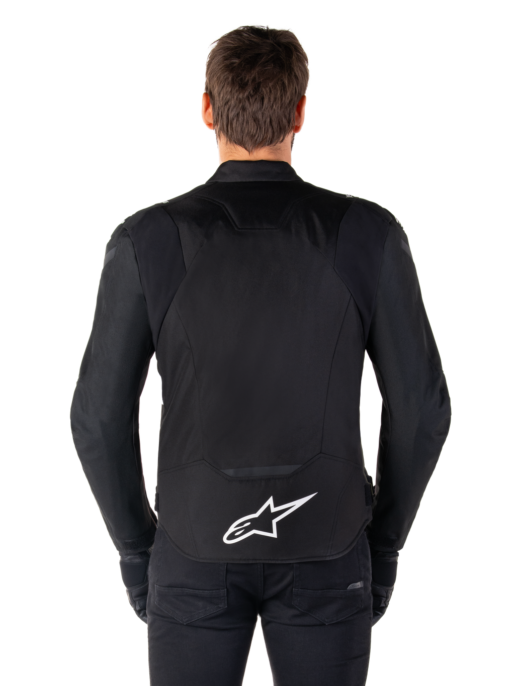 Alpinestars T-Jaws V4 Waterproof Jacket, zwarte motorjas vanaf de achterkant gezien, voorzien van een wit Alpinestars-logo op de onderrug, verlengde achterzijde voor dekking, gedragen door model met zwarte broek en handschoenen, strak sportief textielontwerp