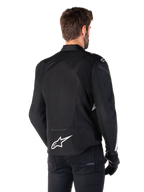 Alpinestars T-Jaws V4 Waterproof Jacket, zwart en wit, achteraanzicht, textiele sportmotorjas met wit logo op de onderrug, gedragen met zwarte handschoenen en broek, voorzien van een herzien sportief silhouet