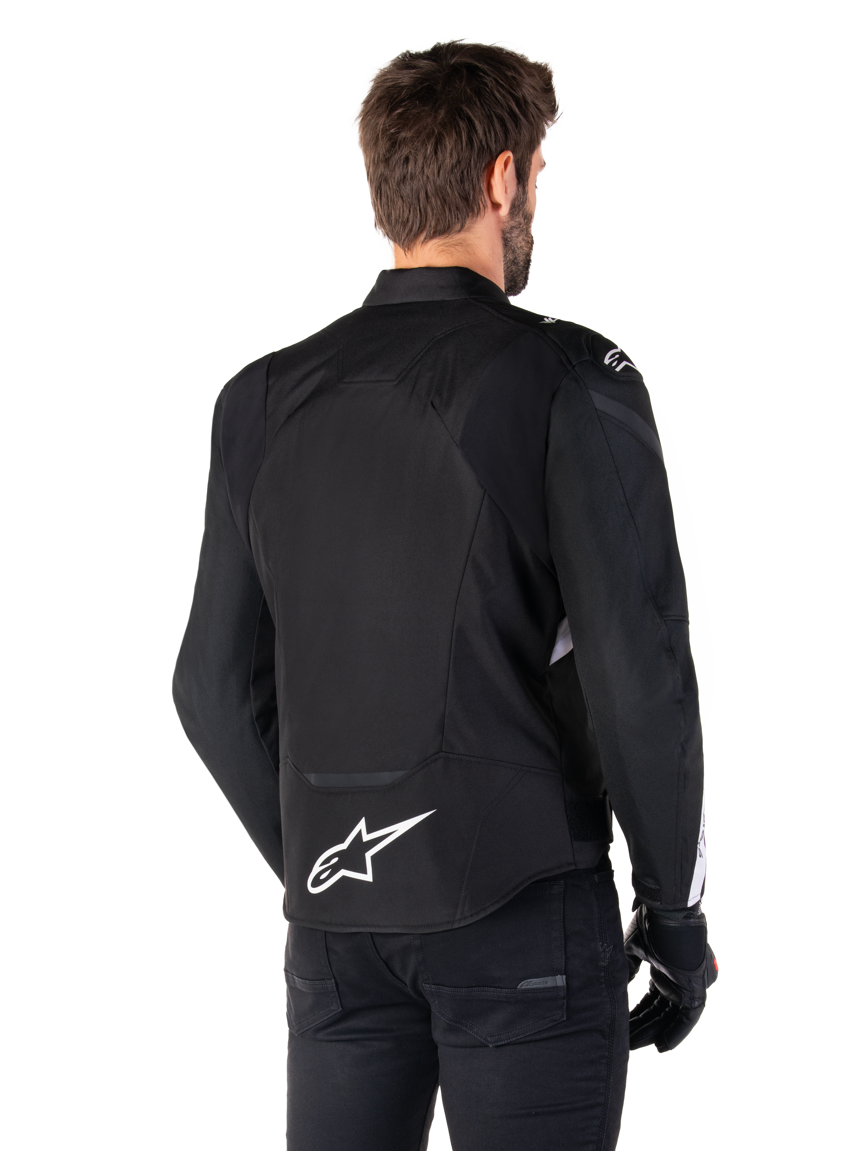Alpinestars T-Jaws V4 Waterproof Jacket, zwart en wit, achteraanzicht, textiele sportmotorjas met wit logo op de onderrug, gedragen met zwarte handschoenen en broek, voorzien van een herzien sportief silhouet