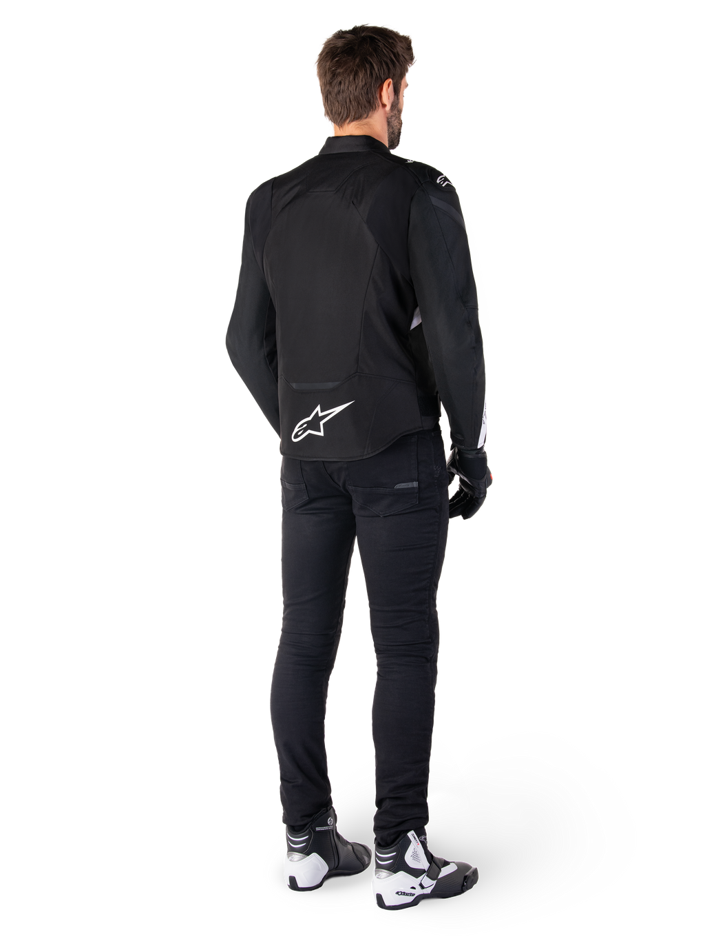 Alpinestars T-Jaws V4 Waterproof Jacket, zwart en wit, achteraanzicht met wit sterlogo op de onderrug, gedragen door model met zwarte motorbroek, zwarte handschoenen en wit-zwarte motorlaarzen