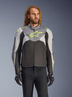 Alpinestars T-Jaws V4 Waterproof Jacket worn by a male model, Black Ice Gray and Dark Gray with Neon Yellow accents, featuring a prominent yellow star logo on the chest, styled with black pants and riding gloves, sport-fit textile motorcycle jacket