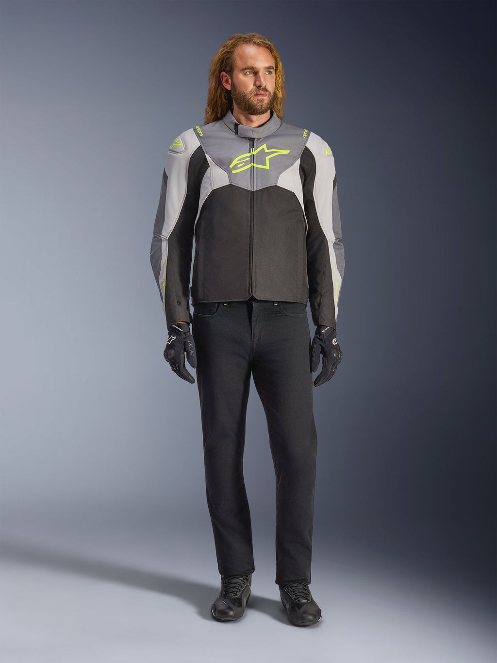 Alpinestars T-Jaws V4 Waterproof Jacket in Black Ice Gray Dark Gray with neon yellow accents, worn by a male model, featuring a sporty silhouette, technical textile construction, and prominent chest logo, styled with black riding pants and gloves