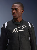 Alpinestars T-SP 1 V2 Waterproof Jacket worn by a model, black and white textile motorcycle jacket, large white Alpinestars logo and T-SP-1 branding on the chest, sporty design with protective shoulder sliders