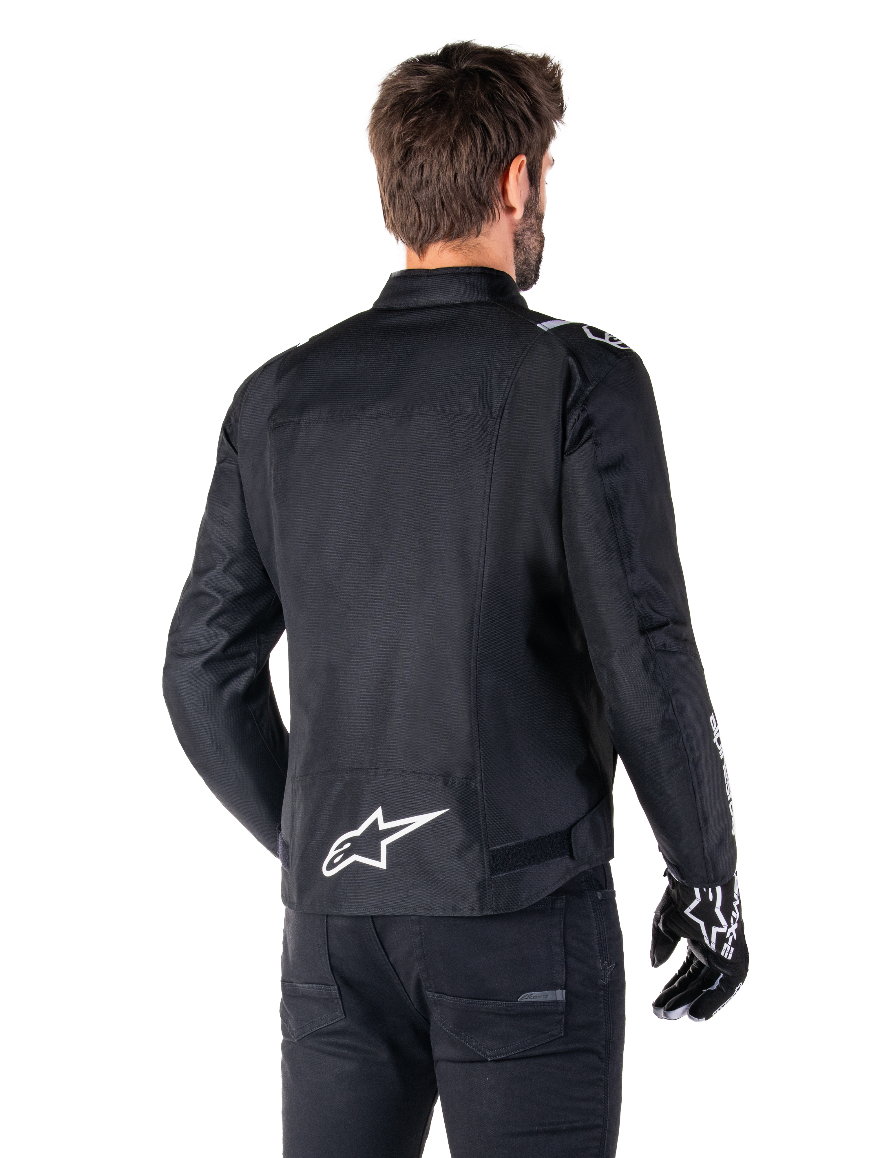 Alpinestars T-SPS V2 Waterproof Jacket, Black and White, rear view of a male rider wearing the jacket, white Alpinestars logo on the lower back, sport cut textile construction, worn with black riding pants and gloves