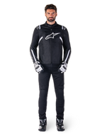 Alpinestars T-SPS V2 Waterproof Jacket, Black and White, worn by male model with black pants and matching gloves, featuring white Alpinestars logo on chest and accents on sleeves, sport-cut silhouette for all-weather motorcycle riding