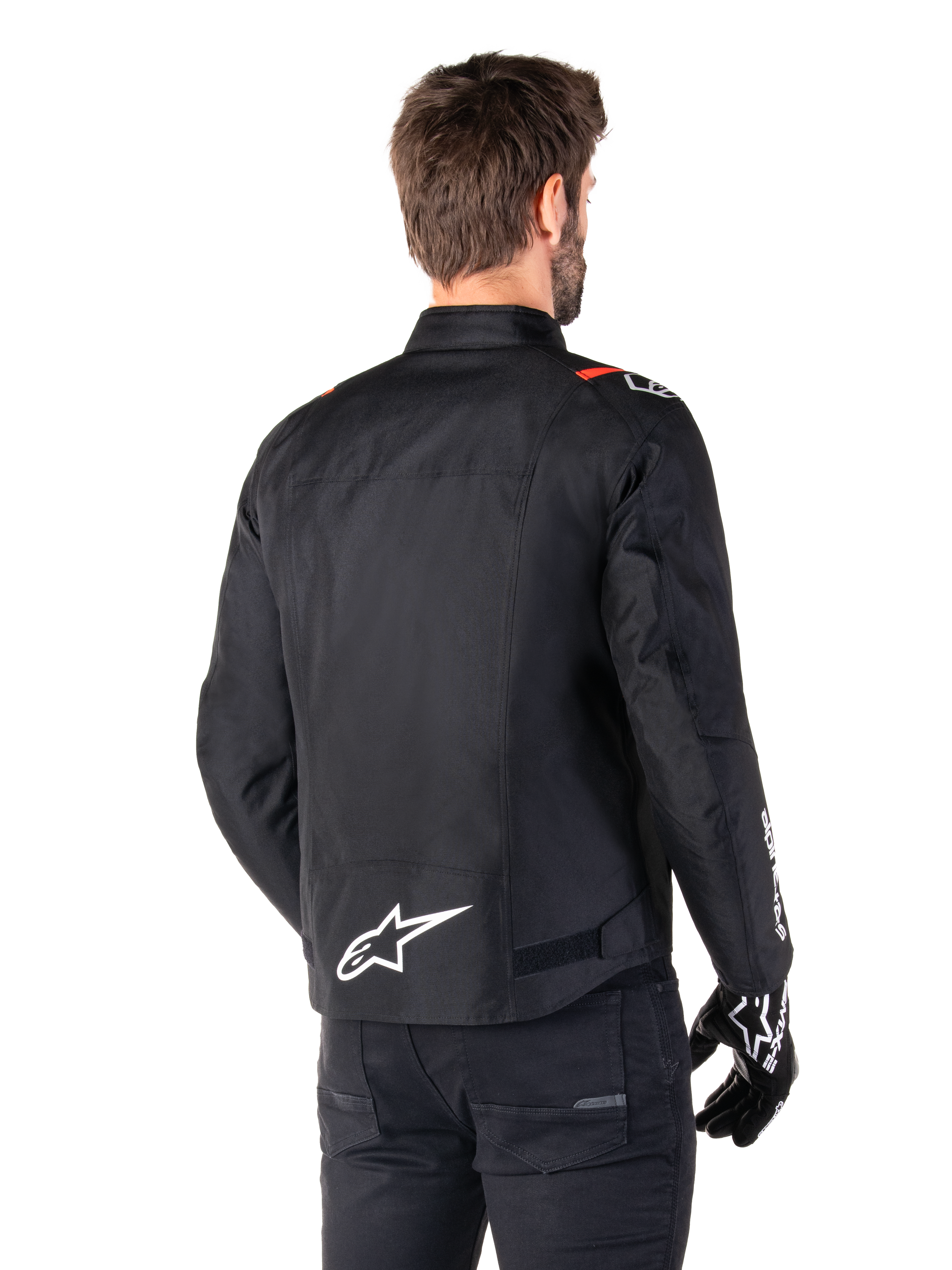 Alpinestars T-SPS V2 Waterproof Jacket, Black White Red Fluo, rear view, featuring white Alpinestars logo on the lower back and red accents on the shoulders, worn with black riding gloves and pants, sport-style textile motorcycle jacket.