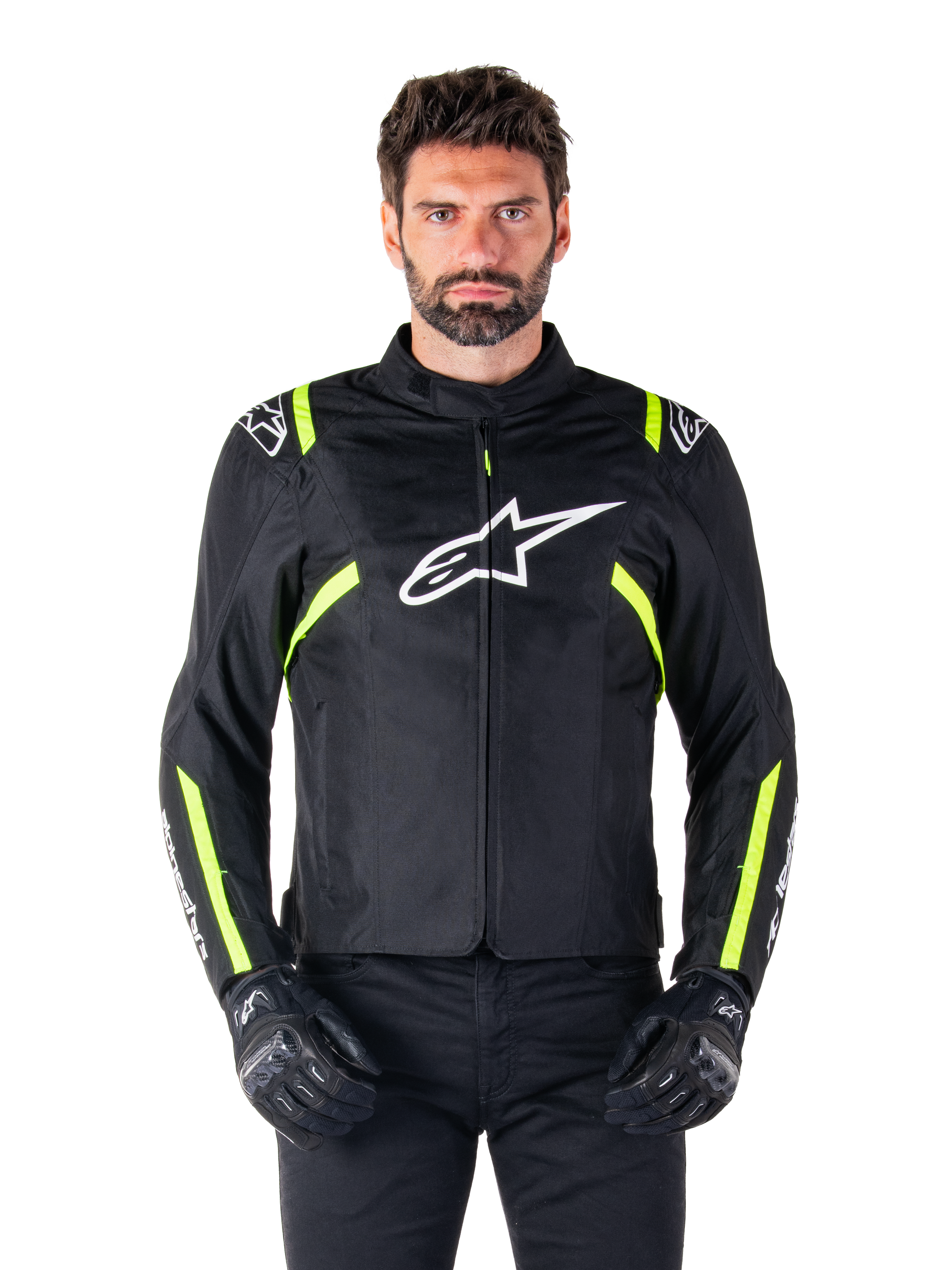Veste imperméable Alpinestars T-SPS V2, veste de moto, noire avec des accents blancs et jaune fluo, portée par un mannequin avec des gants noirs, dotée d'un logo étoile blanc sur la poitrine et de bandes jaune fluo sur les manches et les épaules, équipement textile de style sport pour rouler par tous les temps