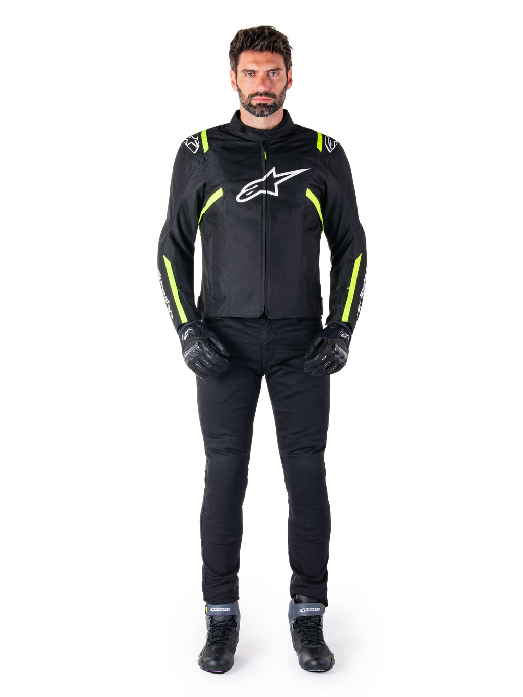 Veste imperméable Alpinestars T-SPS V2, noir, blanc et jaune fluo, portée par un mannequin avec un pantalon et des gants de moto noirs, arborant un logo Alpinestars blanc sur la poitrine et des accents fluorescents sur les épaules et les manches, équipement de moto à coupe sport