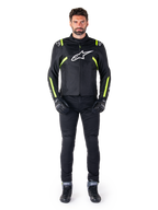 Veste imperméable Alpinestars T-SPS V2, noir, blanc et jaune fluo, portée par un mannequin avec un pantalon et des gants de moto noirs, arborant un logo Alpinestars blanc sur la poitrine et des accents fluorescents sur les épaules et les manches, équipement de moto à coupe sport