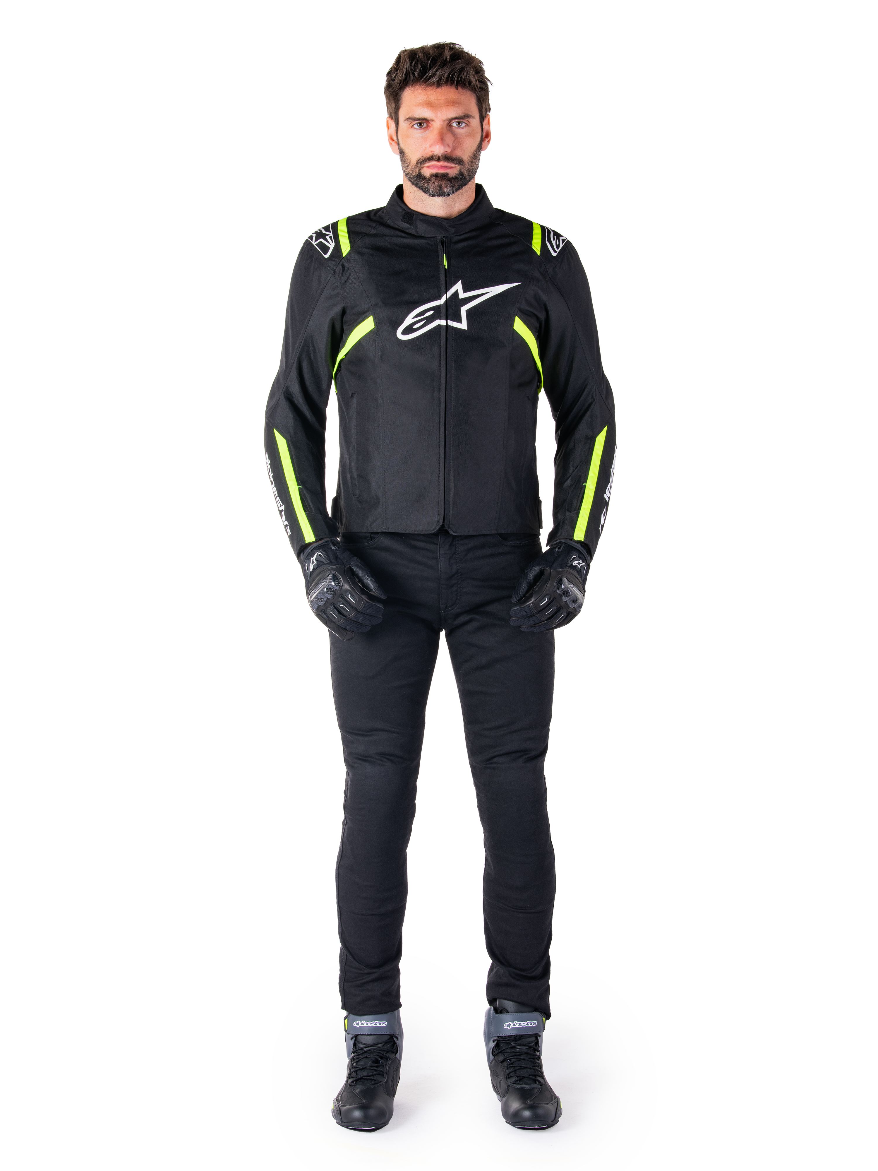 Veste imperméable Alpinestars T-SPS V2, noir, blanc et jaune fluo, portée par un mannequin avec un pantalon et des gants de moto noirs, arborant un logo Alpinestars blanc sur la poitrine et des accents fluorescents sur les épaules et les manches, équipement de moto à coupe sport