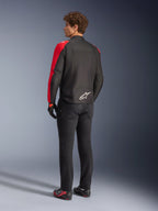 Alpinestars T-SPS V2 Wasserdichte Jacke in Schwarz und Red Fluo, Rückansicht am Modell, getragen mit schwarzer Motorradhose und Motorradschuhen, mit weißem Alpinestars-Logo auf dem unteren Rücken, sportlich geschnittenes Textiljacken-Design.