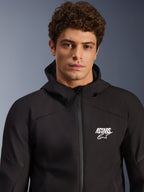 Männliches Model trägt Alpinestars Aeroshell Waterproof Jacke, schwarzer Textil-Softshell-Hoodie, weißes ASTARS-Logo auf der Brust, wasserdichter Frontreißverschluss, modernes Studioporträt für Motorrad-Straßenbekleidung.