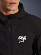 Alpinestars Aeroshell Waterproof Jacke, schwarze Motorrad-Softshelljacke, Nahaufnahme des Brustbereichs mit weißem ASTARS Stern-Logo und wasserdichtem Frontreißverschluss, integrierte Kapuze, modernes sportliches Design