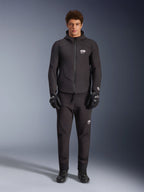 Männliches Model in schwarzer Alpinestars Aeroshell Waterproof Jacke, kombiniert mit passender technischer Hose und Motorradhandschuhen, Softshell-Design mit Kapuze und weißen Logo-Akzenten, modernes, vom Motorsport inspiriertes Outfit für die Straße