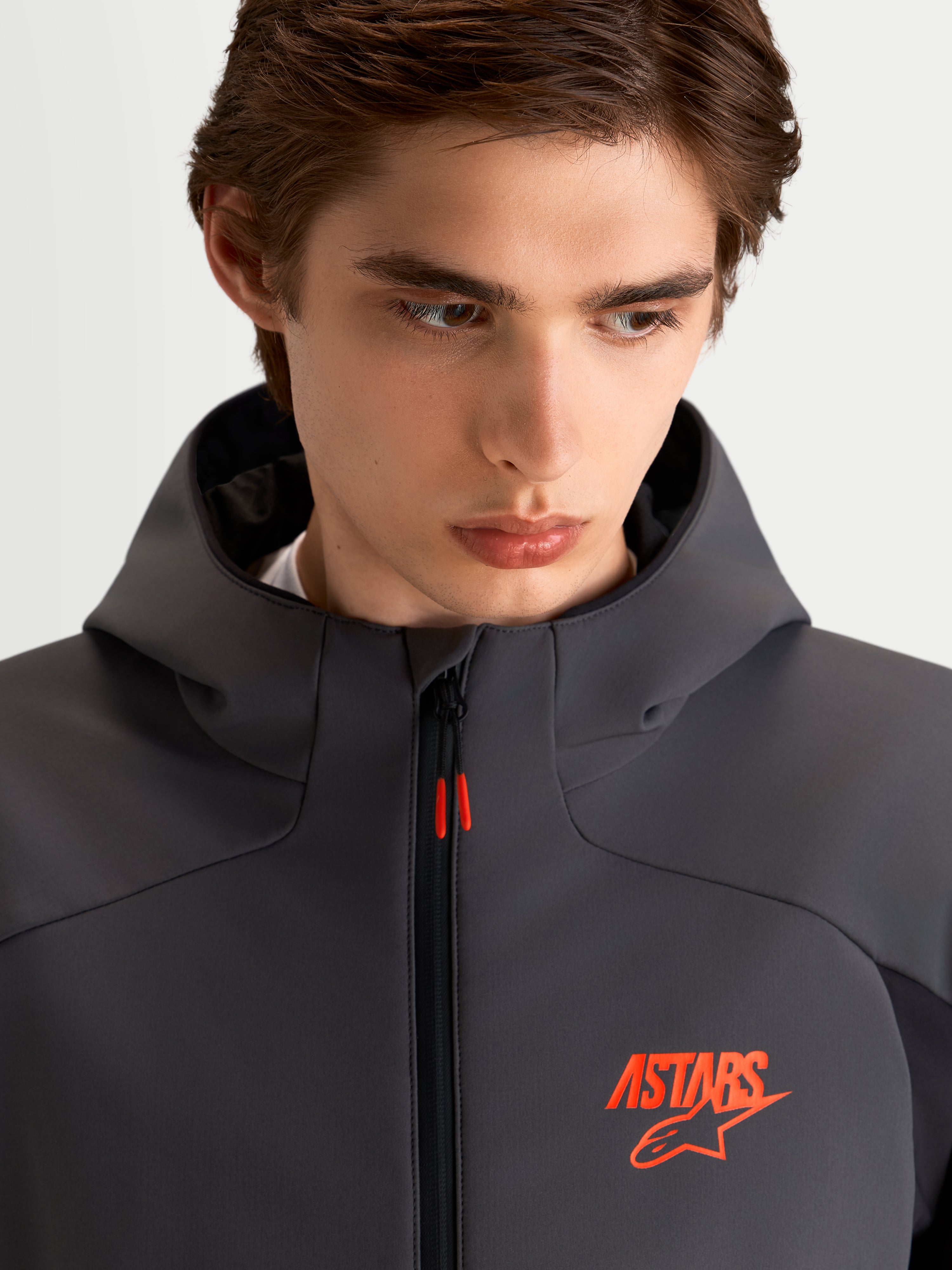 Alpinestars Aeroshell WP jas, heren motor sport softshell jas in zwart en donkergrijs, met capuchon en oranje ASTARS-logo, close-up van model