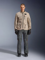 Veste Alpinestars Borrego Drystar®, veste de moto d'aventure, Warm Gray, portée par un mannequin avec un pantalon de moto gris foncé et des gants noirs, dotée de multiples poches cargo et d'une construction textile durable avec un aspect classique en toile cirée.