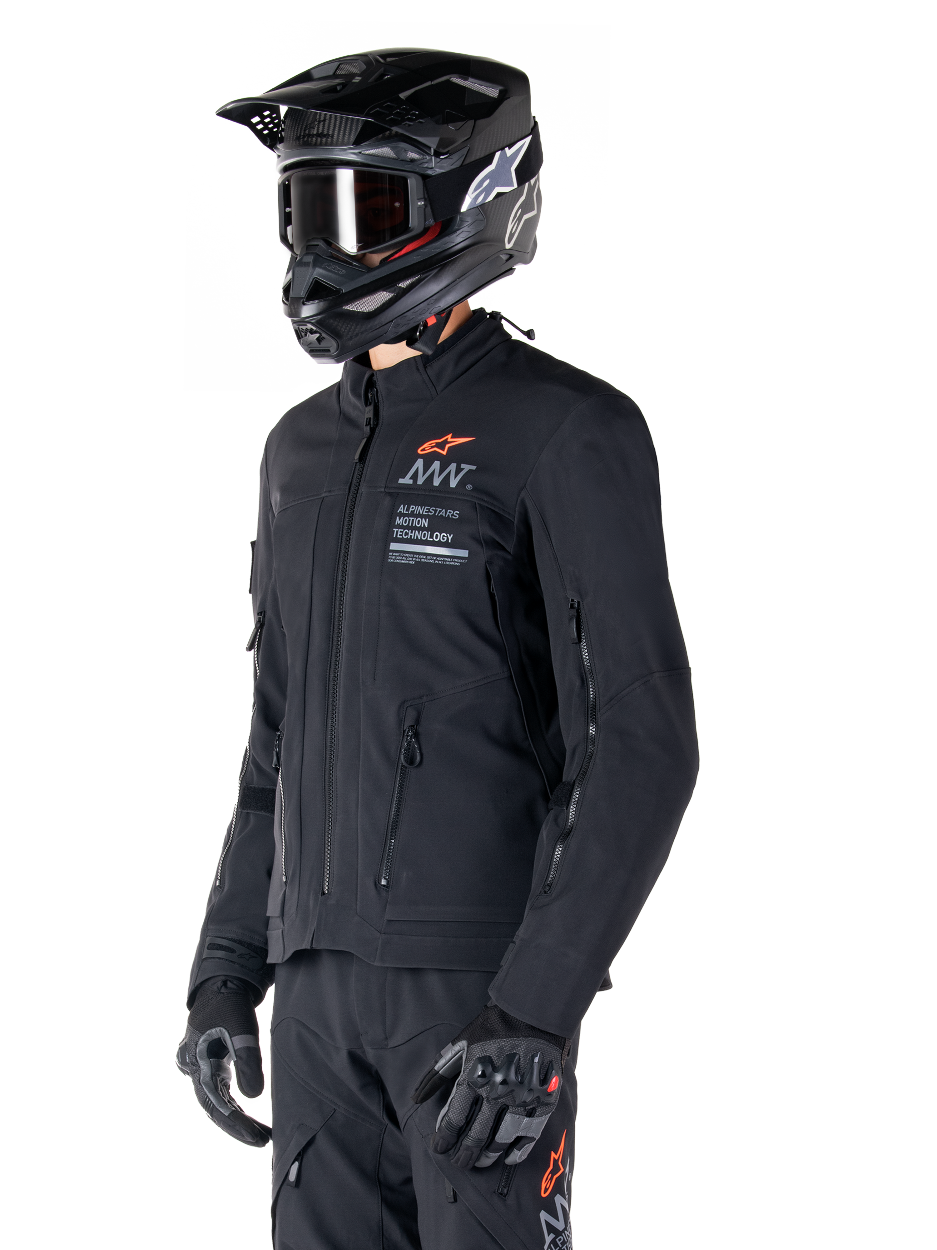 Alpinestars AMT-8 Stretch Drystar® XF Jacke, Schwarz, getragen von einem Fahrer mit passender Adventure-Hose und Handschuhen, mit einem schwarzen Motocross-Helm und einer Schutzbrille, Belüftungsöffnungen mit Reißverschluss an Brust und Armen, Alpinestars Motion Technology-Branding mit einem orangefarbenen Logo, Premium-Adventure-Touring-Ausrüstung.