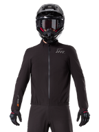 Alpinestars AMT-8 Stretch Drystar® XF Liner, schwarze wasserdichte Motorrad-Innenjacke, mit Frontreißverschluss und elastischem Bund, AMT-Logo auf der Brust und Drystar XF Branding am Ärmel, getragen mit schwarzem Helm und Handschuhen.