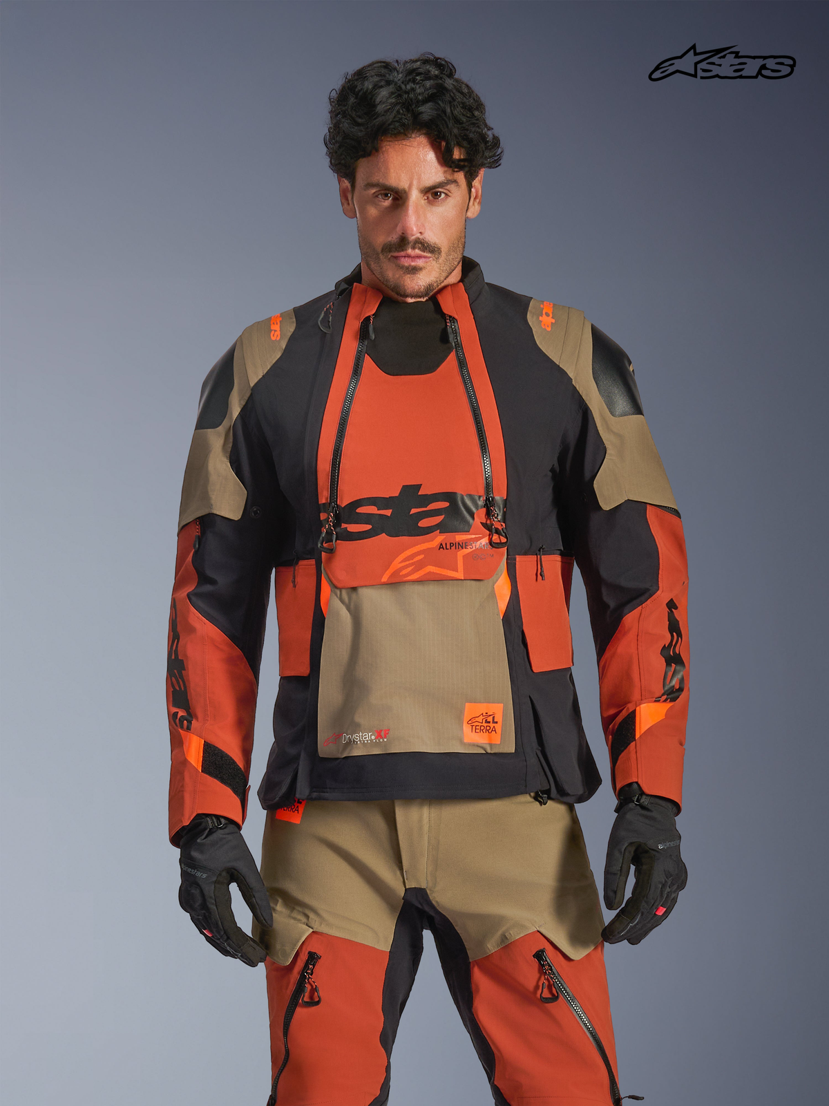 Alpinestars Halo Pro Drystar® XF gelamineerde jas, avontuurlijke motorjas voor heren in walnootbruin, roestoranje en zwart, vooraanzicht op model met bijpassende uitrusting, waterdichte textielconstructie en modulaire ventilatiepanelen