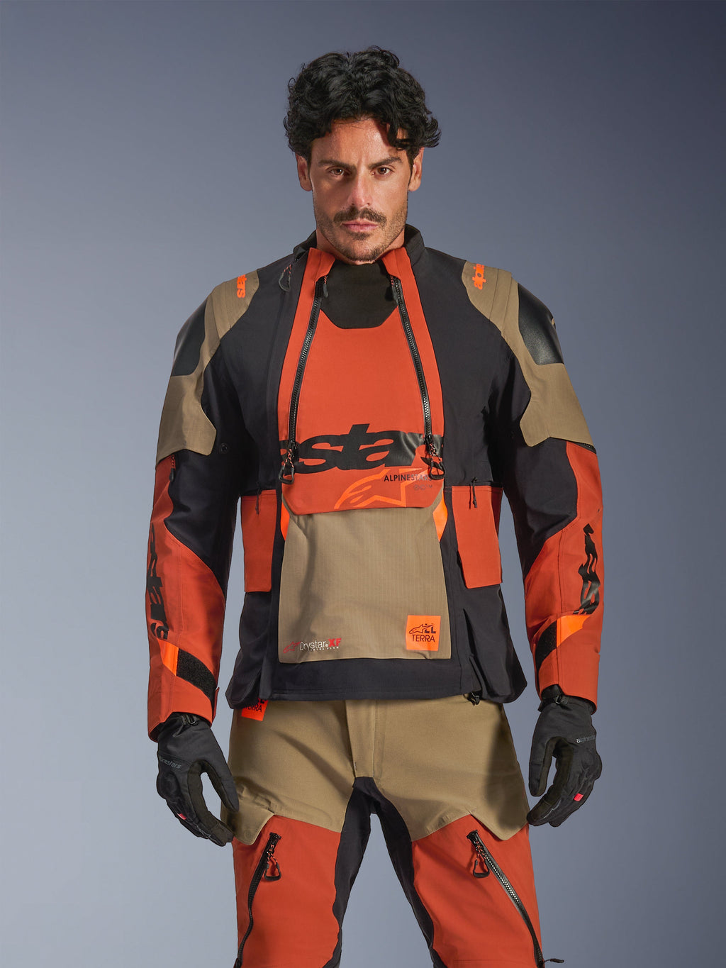 Alpinestars Halo Pro Drystar XF Laminated Jacket, adventure motorjas, Walnut Rust en zwart met tan-accenten, gedragen door een model met bijpassende kleding, vooraanzicht, voorzien van waterdichte gelamineerde constructie en modulaire ventilatiepanelen op de borst, premium all-terrain rijuitrusting