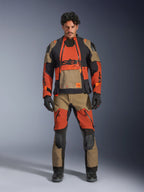 Mannelijk model draagt de Alpinestars Halo Pro Drystar® XF Gelamineerde Jas en bijpassende broek in Walnut Rust Black, modulaire adventure motoruitrusting voorzien van ventilatiepanelen aan de voorzijde en ritsen, gecombineerd met zwarte motorhandschoenen en laarzen.