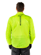 Veste Alpinestars Hurricane Rain V2, veste de pluie moto, jaune fluo, vue arrière montrant le logo Alpinestars noir vertical au centre du dos, tissu imperméable léger, portée avec un pantalon et des gants de moto noirs